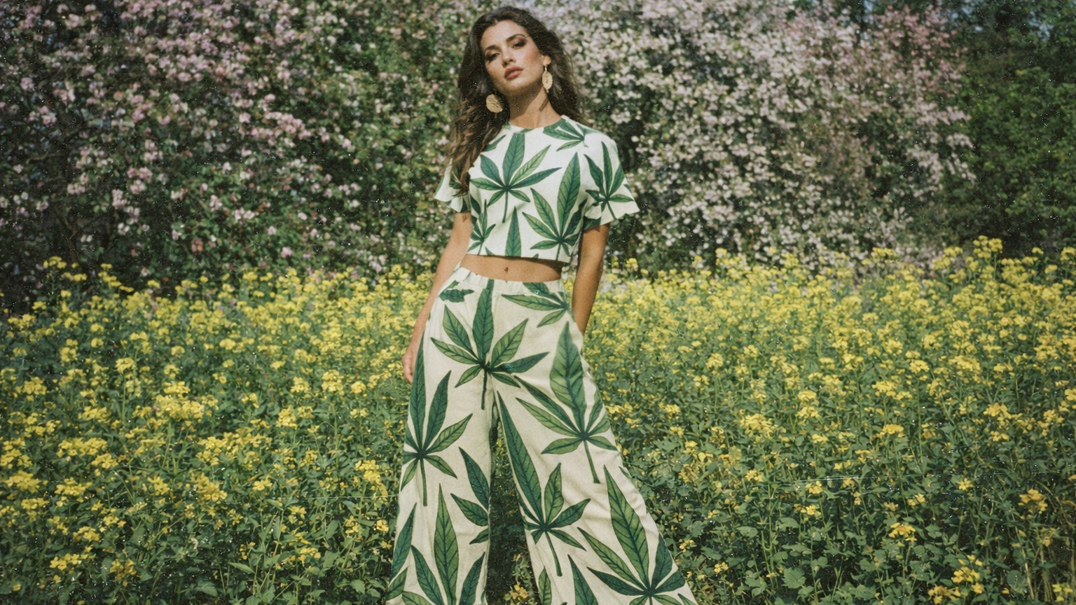 Woman wearing a green and white leaf-patterned outfit standing in a field of yellow flowers.
