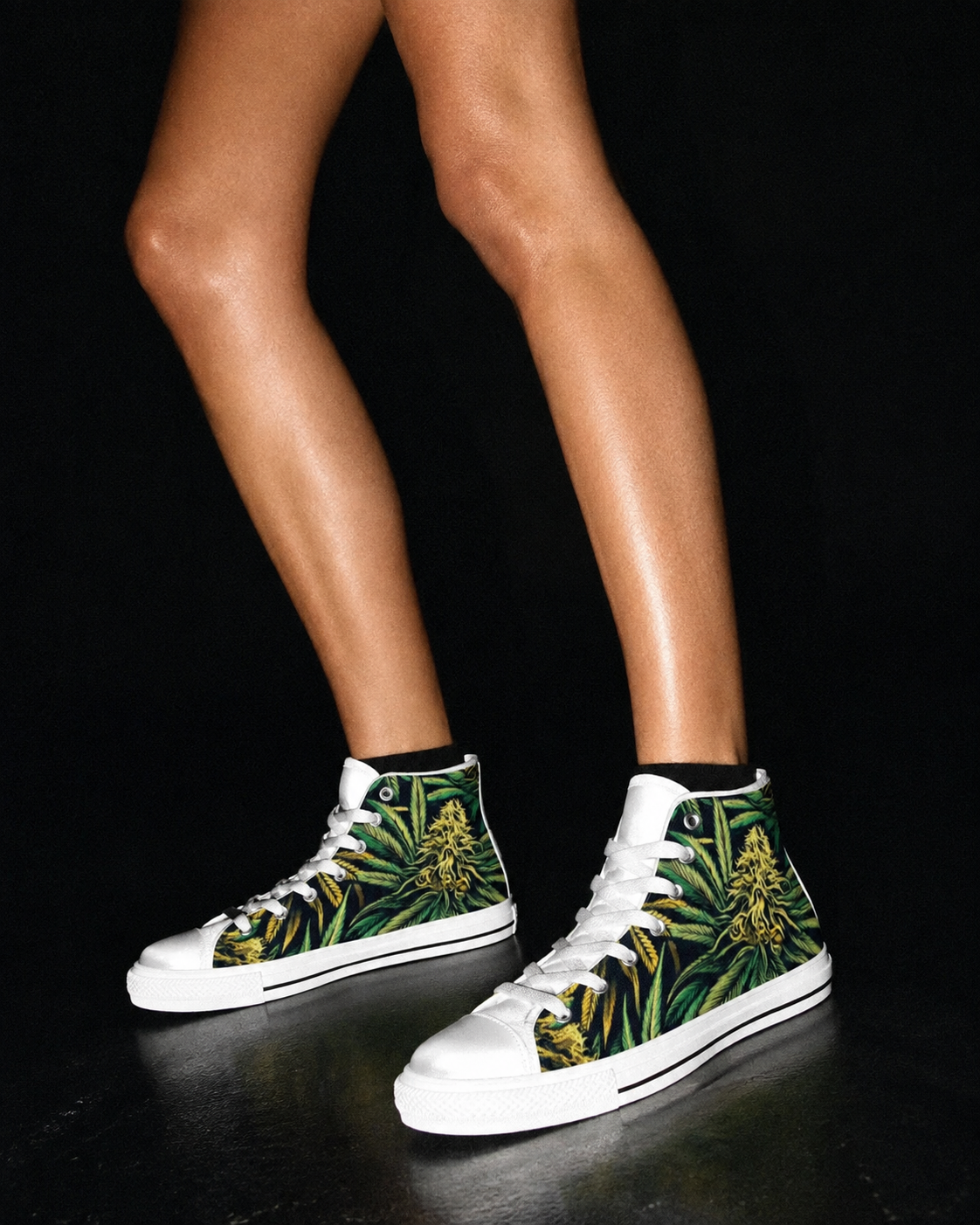 A person wearing white high-top sneakers with a green tropical leaf and yellow flower print, shown from the knees down against a black background.