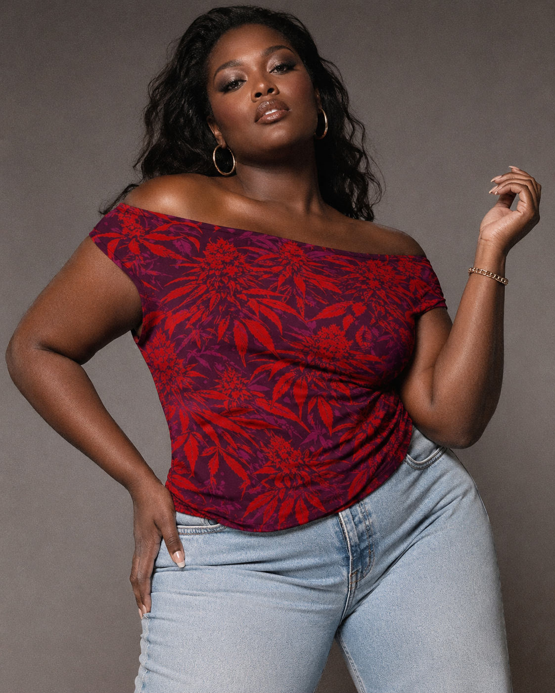 Woman wearing a red and purple floral off-shoulder top and light blue jeans against a gray background