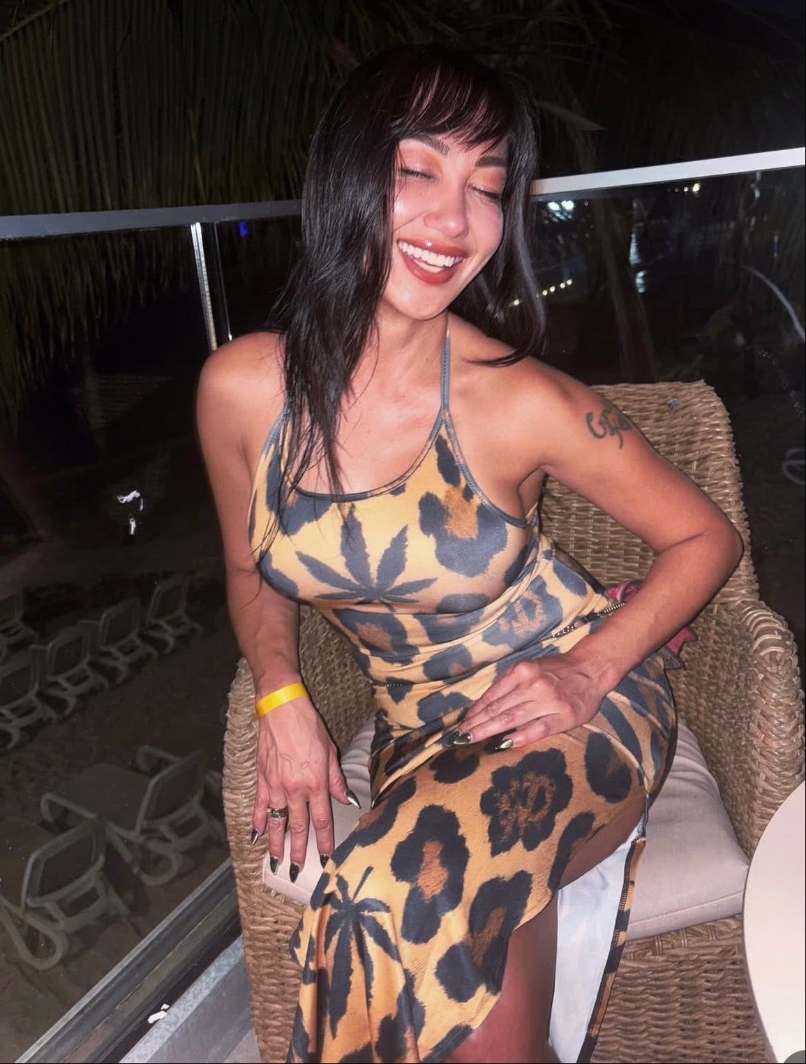 Woman in a leopard print dress sitting on a chair at night.