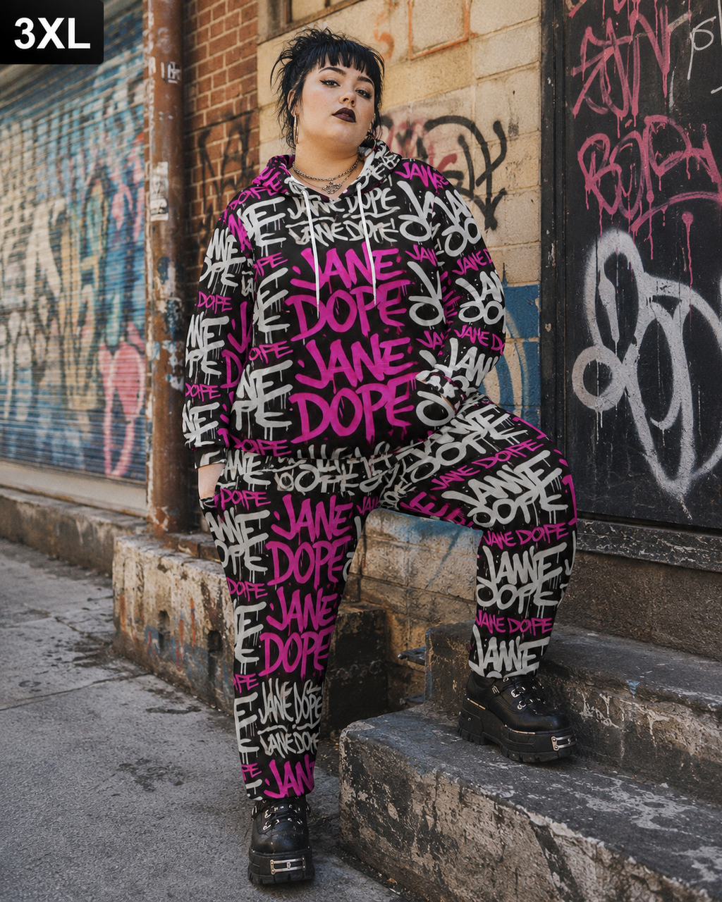 A person wearing a matching oversized hoodie and jogger pants set with a bold graffiti-style print featuring the words 'JANE DOPÉ' in bright pink, black, and white, sitting on concrete steps against a graffiti-covered wall.