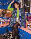 Get Lit Hanukkah Large Scarf worn open across the shoulders, showing its blue botanical and menorah print and long fringed ends.