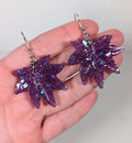 Glitter moonstone cannabis leaf earrings in purple, close-up