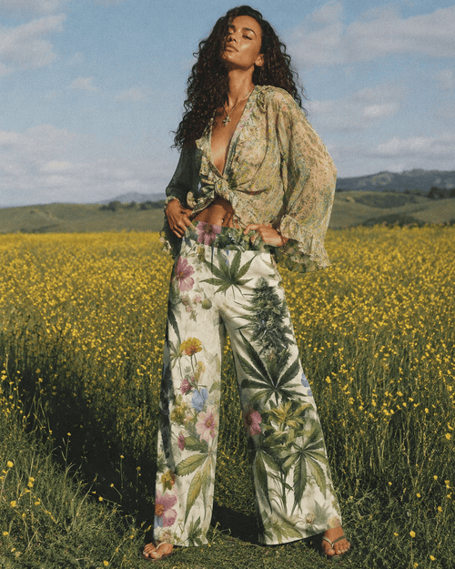 Woman in a floral outfit standing in a field with yellow flowers and green hills in the background