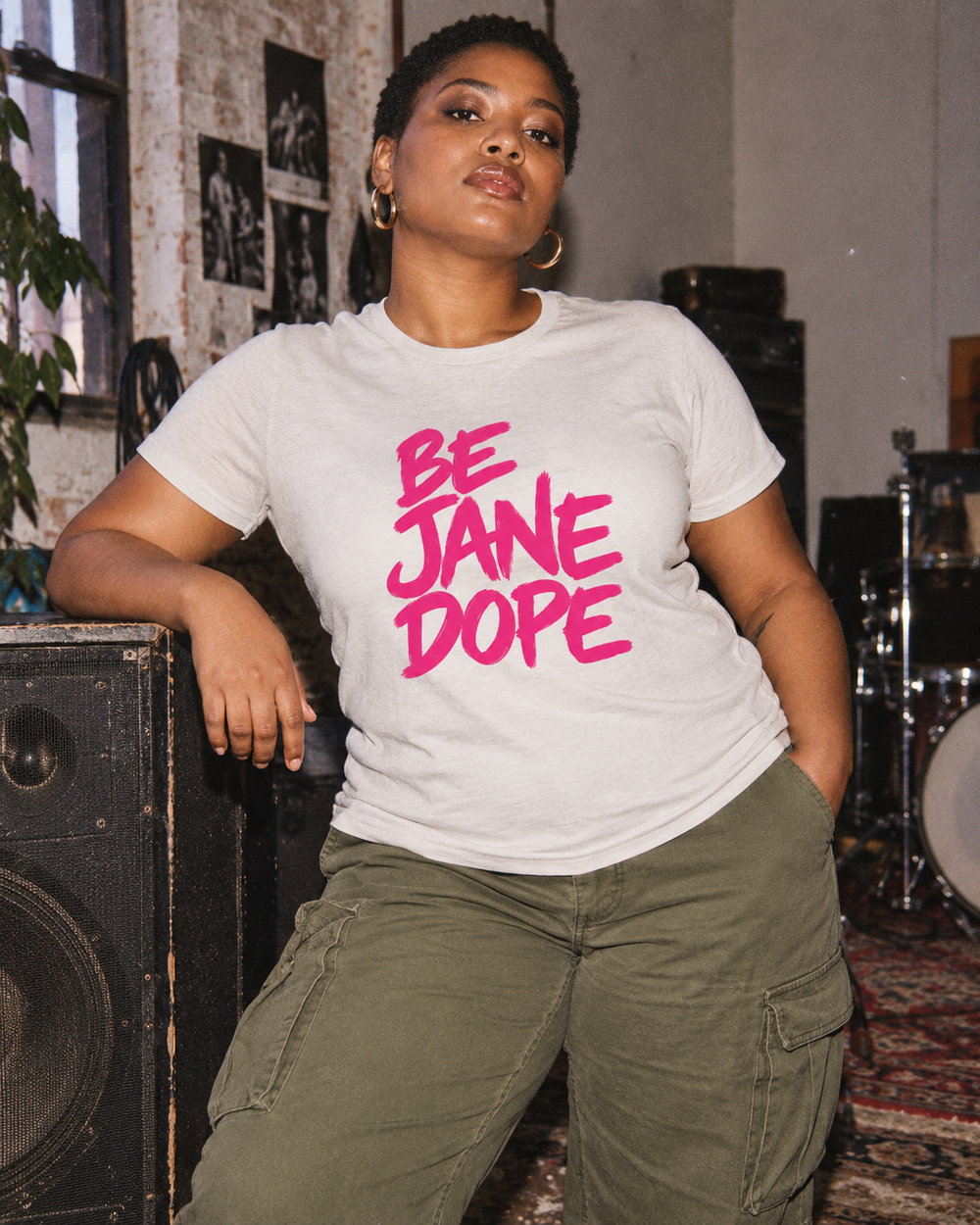 Front of BE JANE DOPE tee with olive cargo trousers beside a vintage speaker.