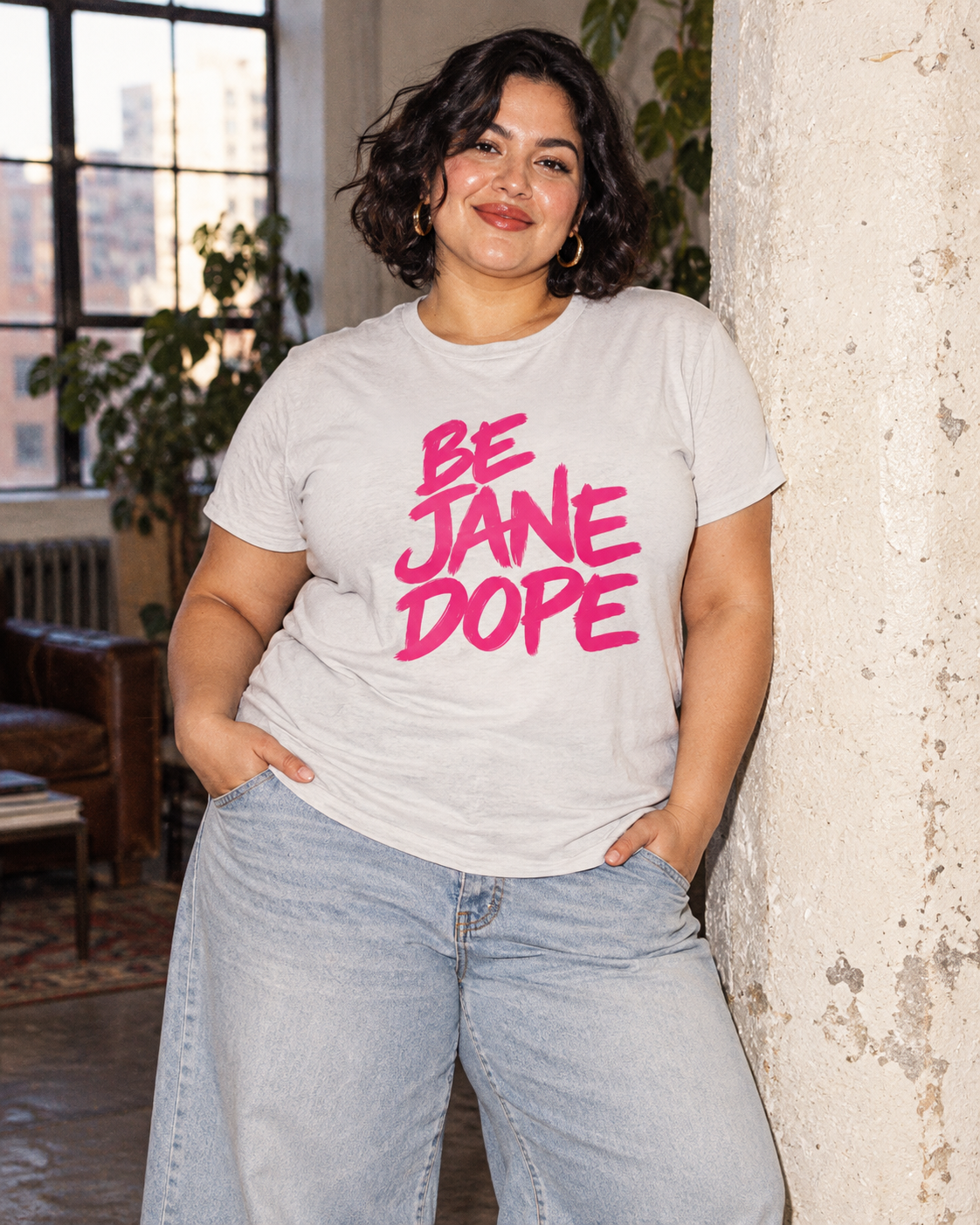 BE JANE DOPE cotton tee with light-wash jeans beside a concrete pillar.