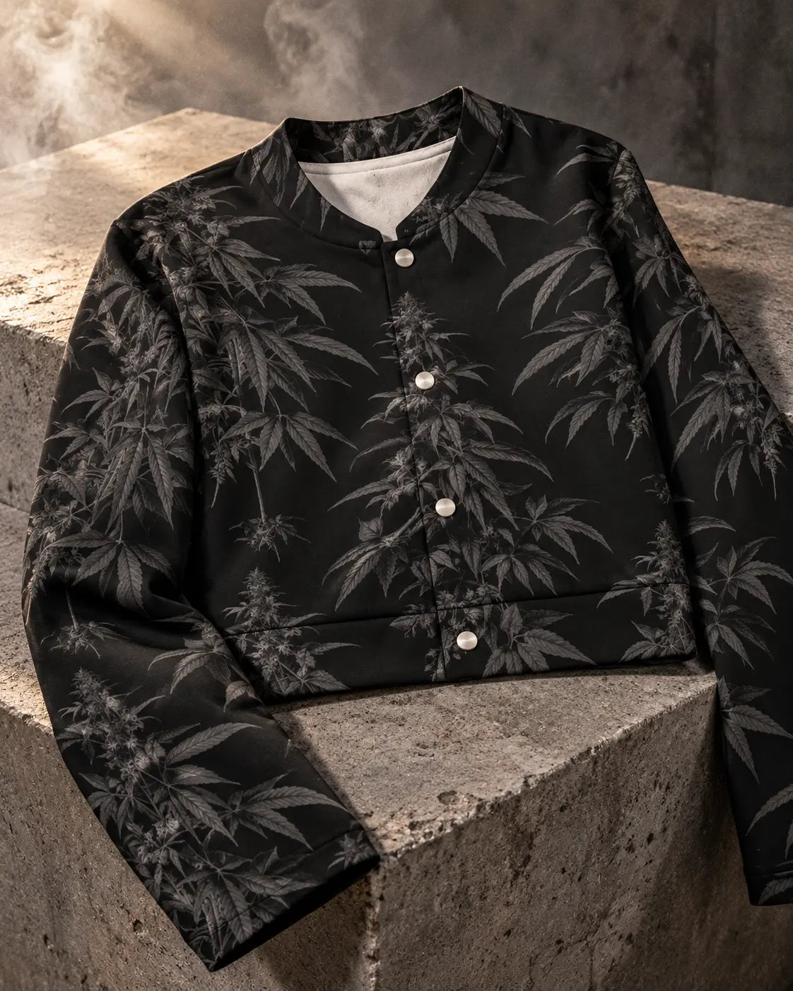 Close-up of Black Widow cropped jacket charcoal botanical print, silver snap fasteners, fabric texture and hem on gray concrete.
