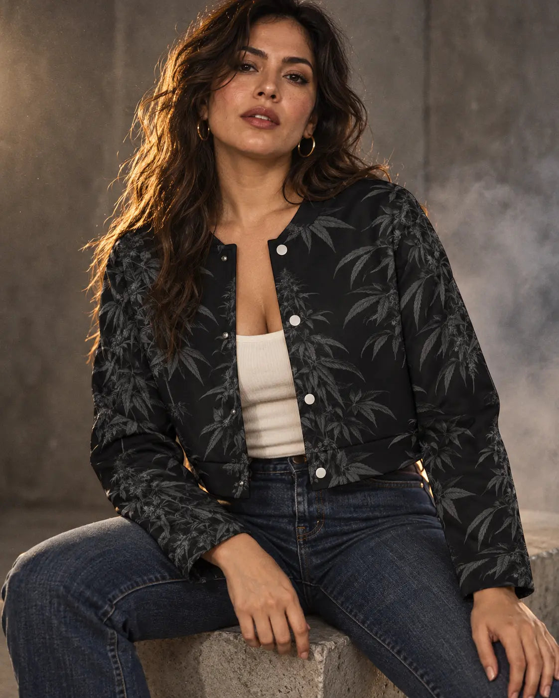 Seated model wearing the Black Widow cropped jacket with a cream camisole and dark denim, showing silver snaps and long sleeves.