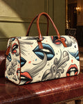 Boujie XL cream travel bag with blue and coral lips and grey smoke print on an oxblood bench.