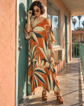 Front view of the Cali burnt-orange botanical kaftan dress, worn with amber sunglasses at a turquoise motel door.