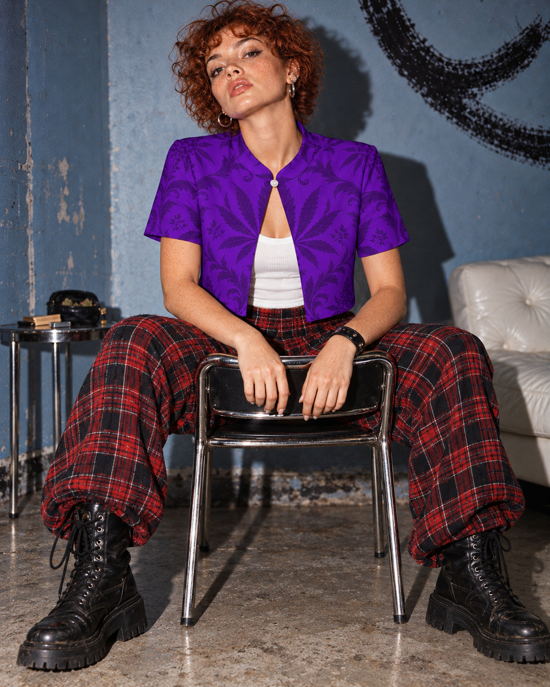 Purple botanical Gelato cropped bolero with a white ribbed tank, red tartan trousers and combat boots; model straddles a chrome chair.