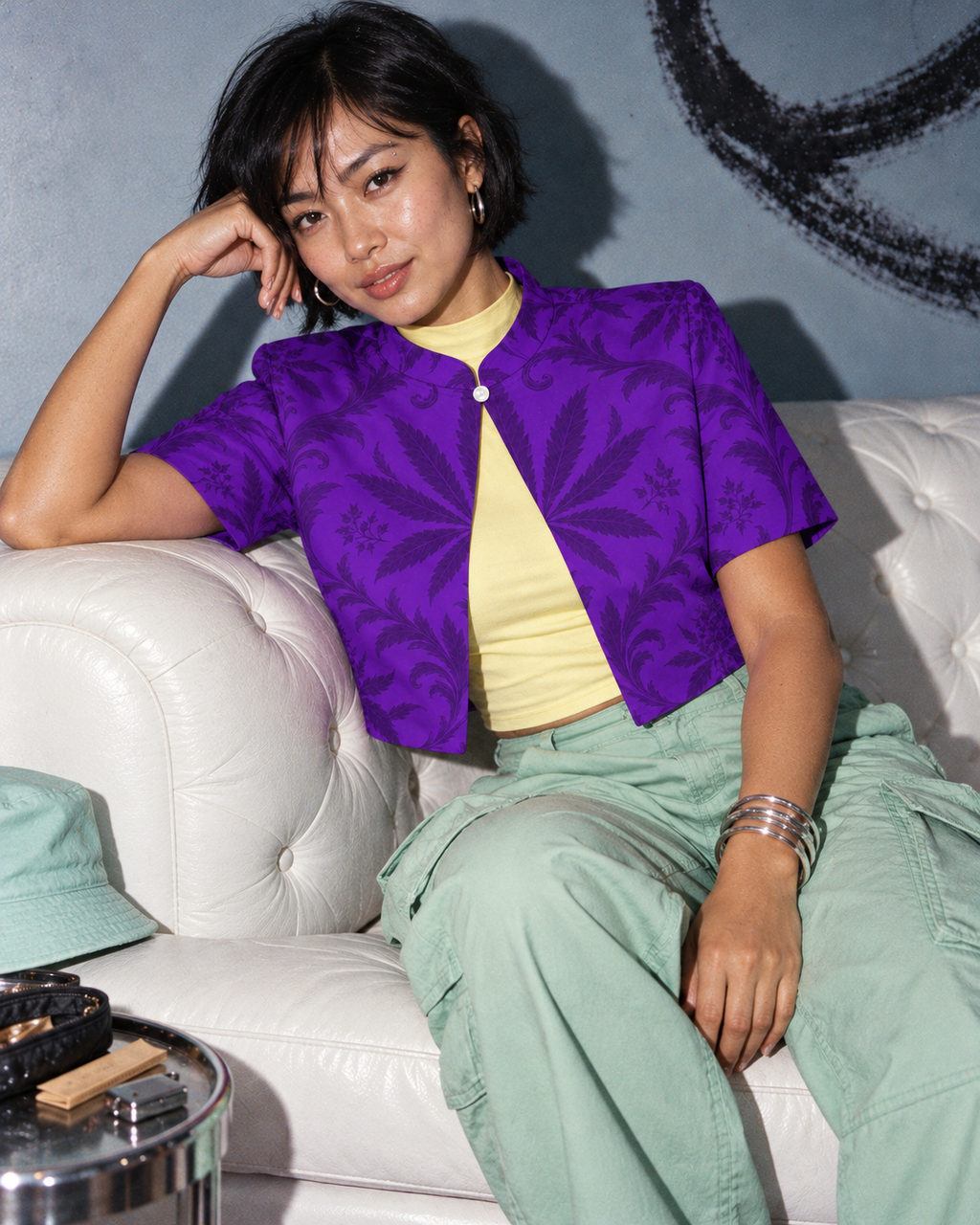 Purple botanical Gelato cropped bolero styled with a lemon top and mint cargo trousers, on a model lounging on a white sofa.