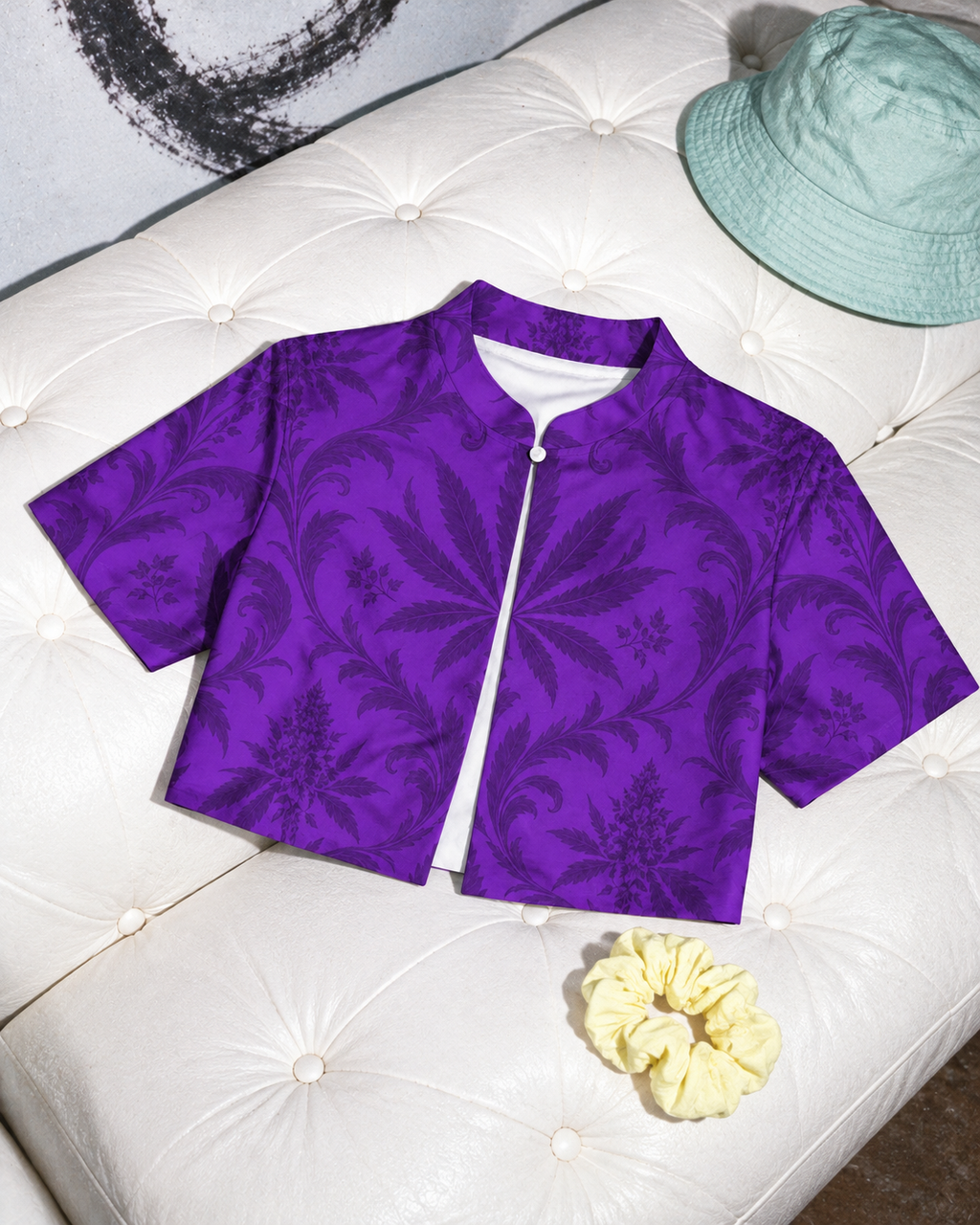 Gelato purple botanical bolero laid front-up on a white tufted sofa, with a mint hat and lemon scrunchie alongside.