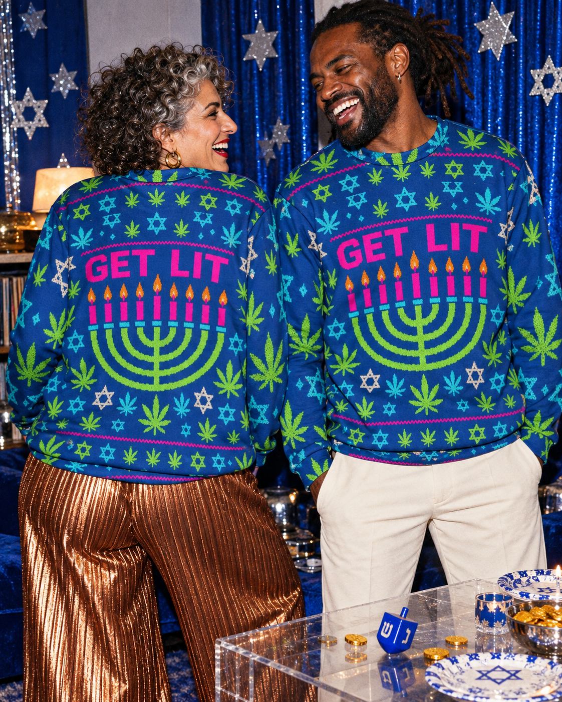 Two models in blue Get Lit Hanukkah sweatshirts showing the back and front artwork beside a festive party table.