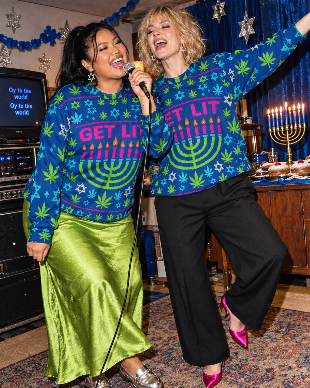 Two models wearing the blue Get Lit Hanukkah sweatshirt at a festive karaoke party, showing the front menorah print.