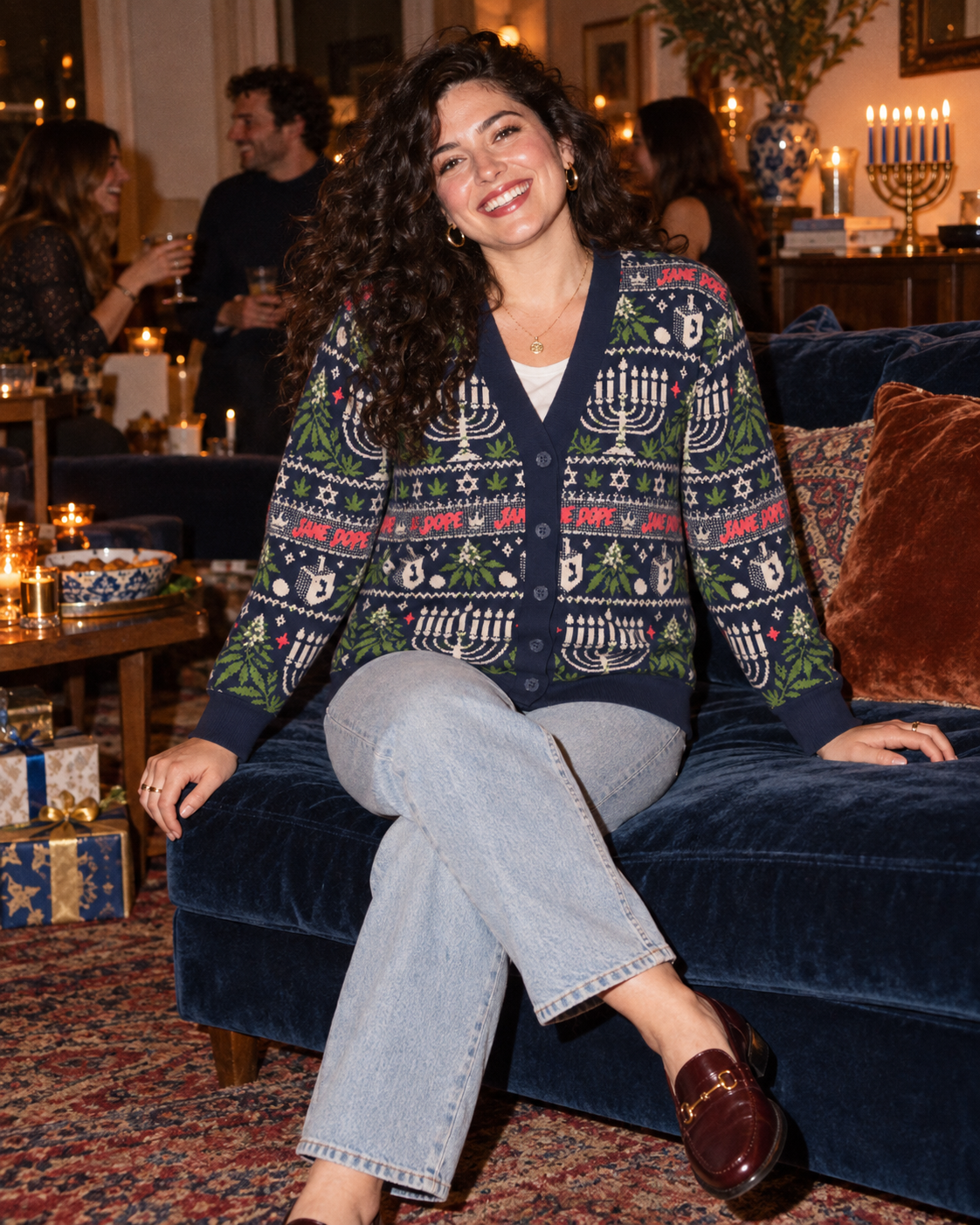 Get Lit cardigan styled with pale jeans, seated on a navy velvet sofa.