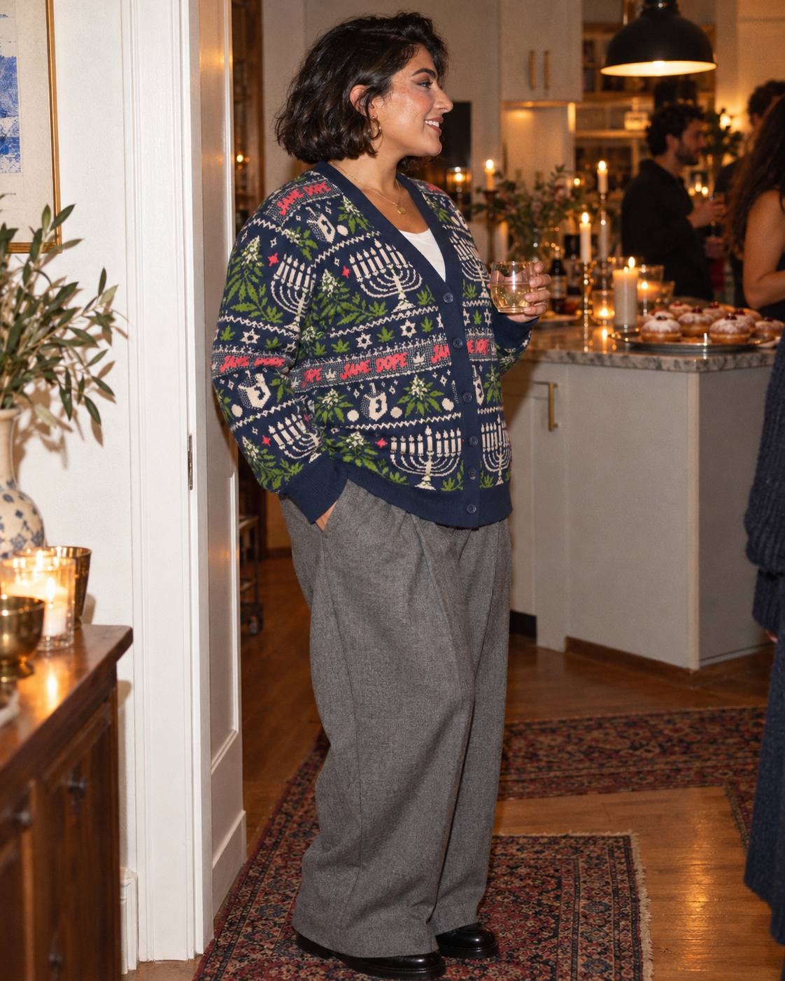 Angled view of Get Lit cardigan with grey wide-leg trousers at a holiday gathering.