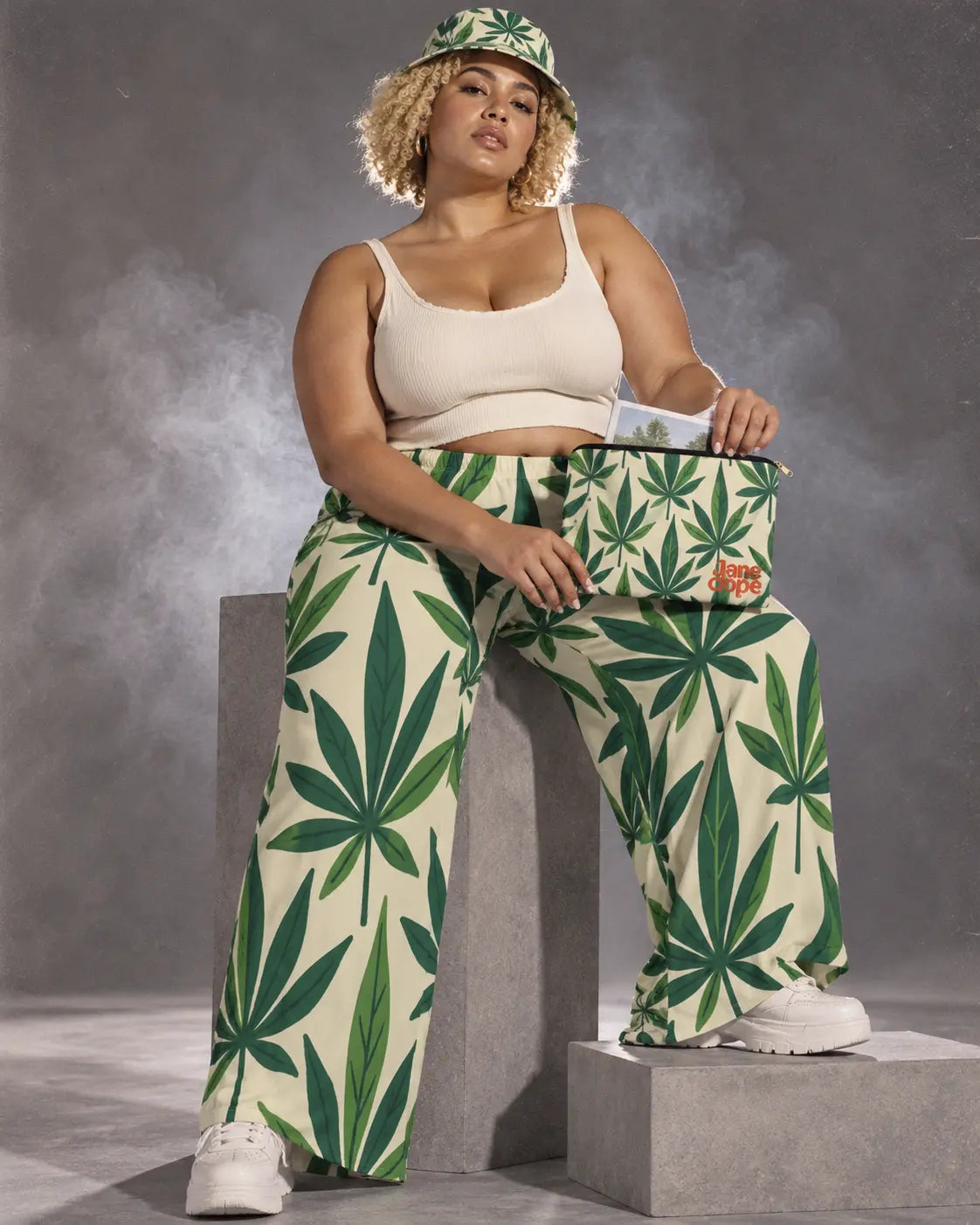 Model seated on a gray plinth in the Grass Kit with an open stash pouch and paper booklet on her thigh.