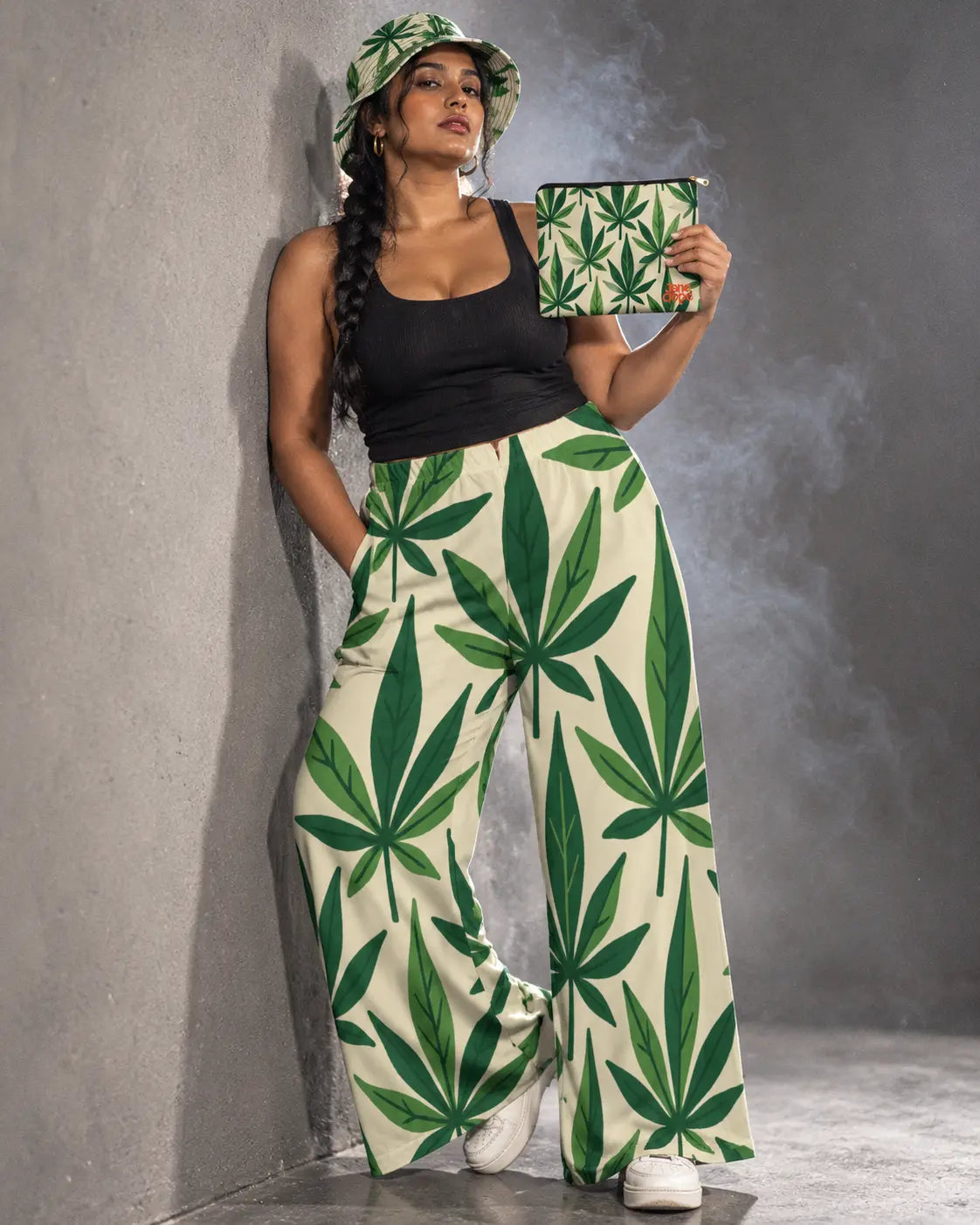 Model leaning against a gray studio wall in the Grass Kit, holding the matching pouch beside her shoulder.