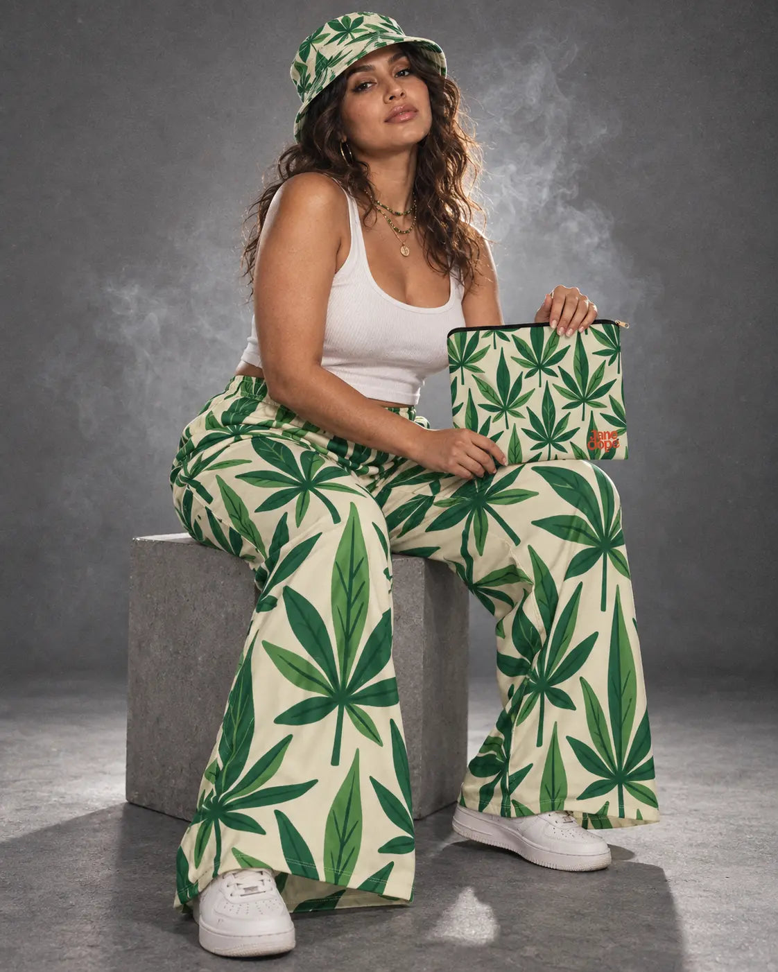 Seated model wearing Grass wide-leg pants and bucket hat with the matching stash pouch upright on her lap.