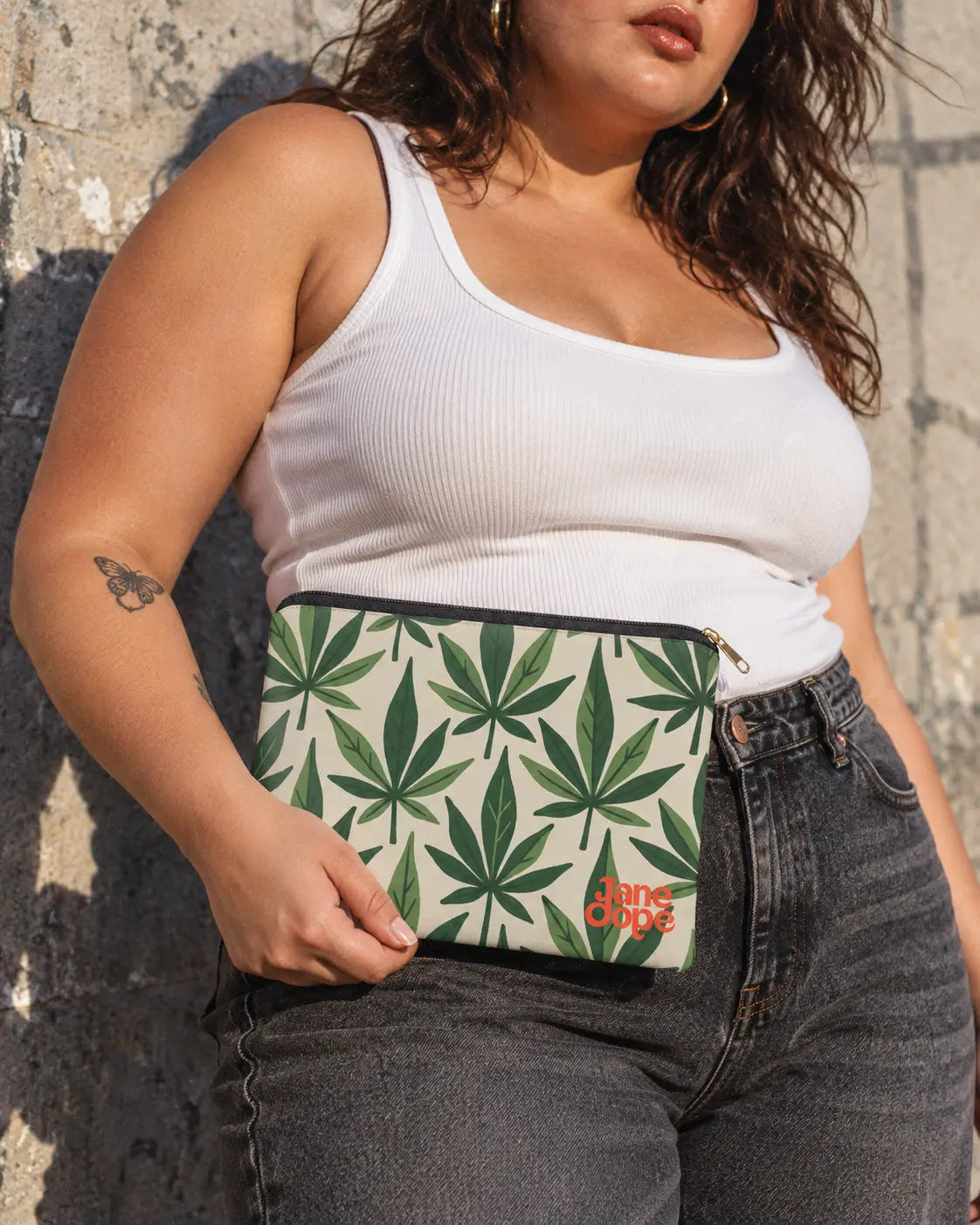 Model holding the Jane Dope Grass leaf-print stash pouch at her hip, styled with a white tank and faded black jeans.