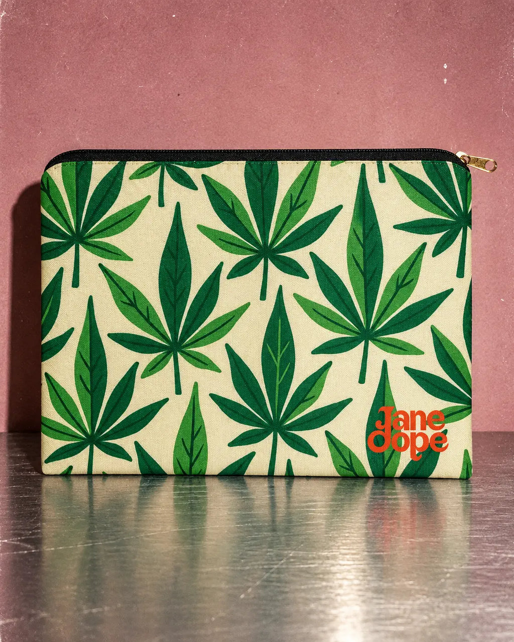Jane Dope Grass stash pouch with green HER.B leaf print, cream background and orange logo on a metal surface.