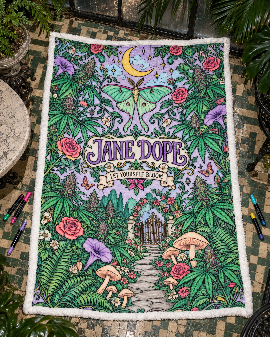 Fully coloured JD Magic blanket inspiration with green foliage, pink roses, a turquoise moth and purple lettering; blanket arrives uncoloured