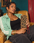 Leopard Clutch Wallet with tan-and-black Herb print and a red wristlet, held upright beside mint streetwear.