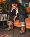 Leopard-and-Herb print booties styled with cuffed denim, a black bomber and gold jewellery in a teal and apricot listening room.