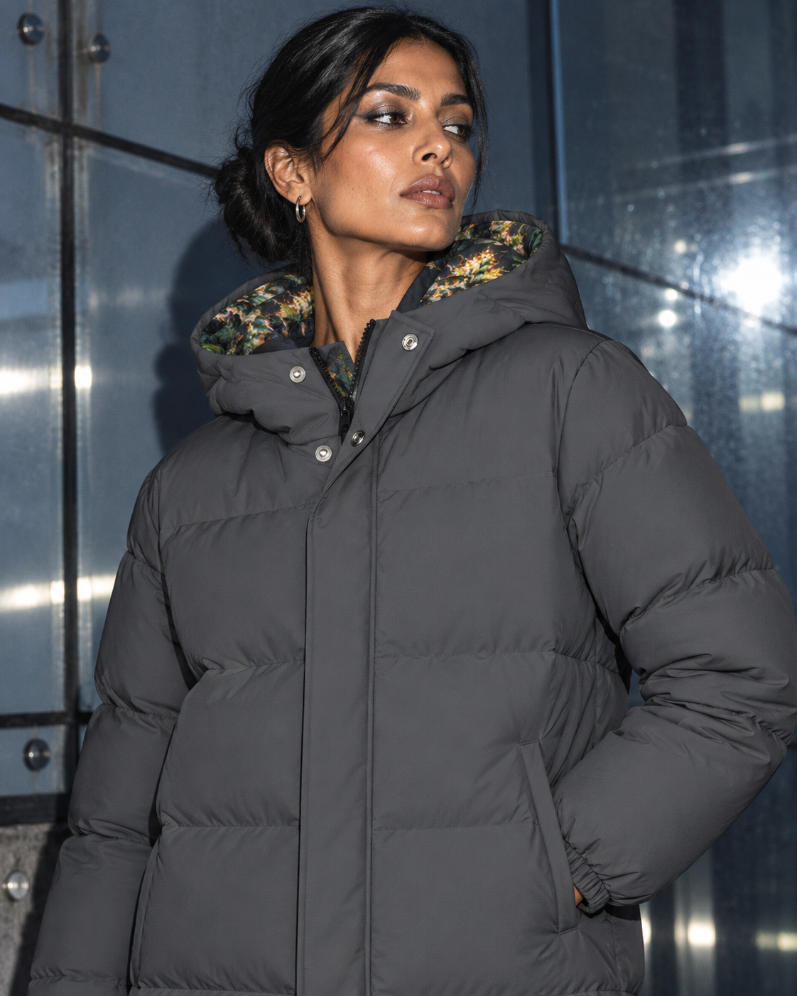 On-body close-up of charcoal down jacket showing padded hood, botanical lining and snap closure