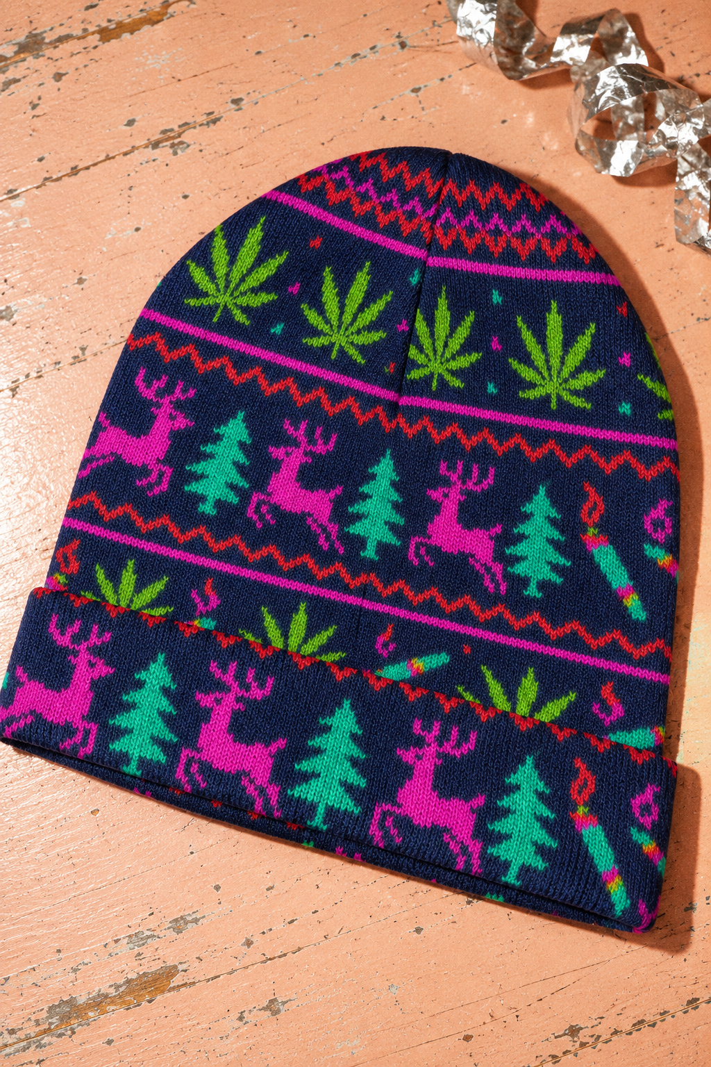 Neon Xmas Beanie with folded cuff, navy polyester knit and bright holiday print on a peach tabletop