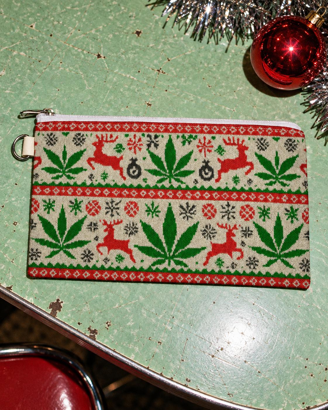 OG Xmas Stash Pouch showing its holiday print, white zip and silver side ring on a mint diner table