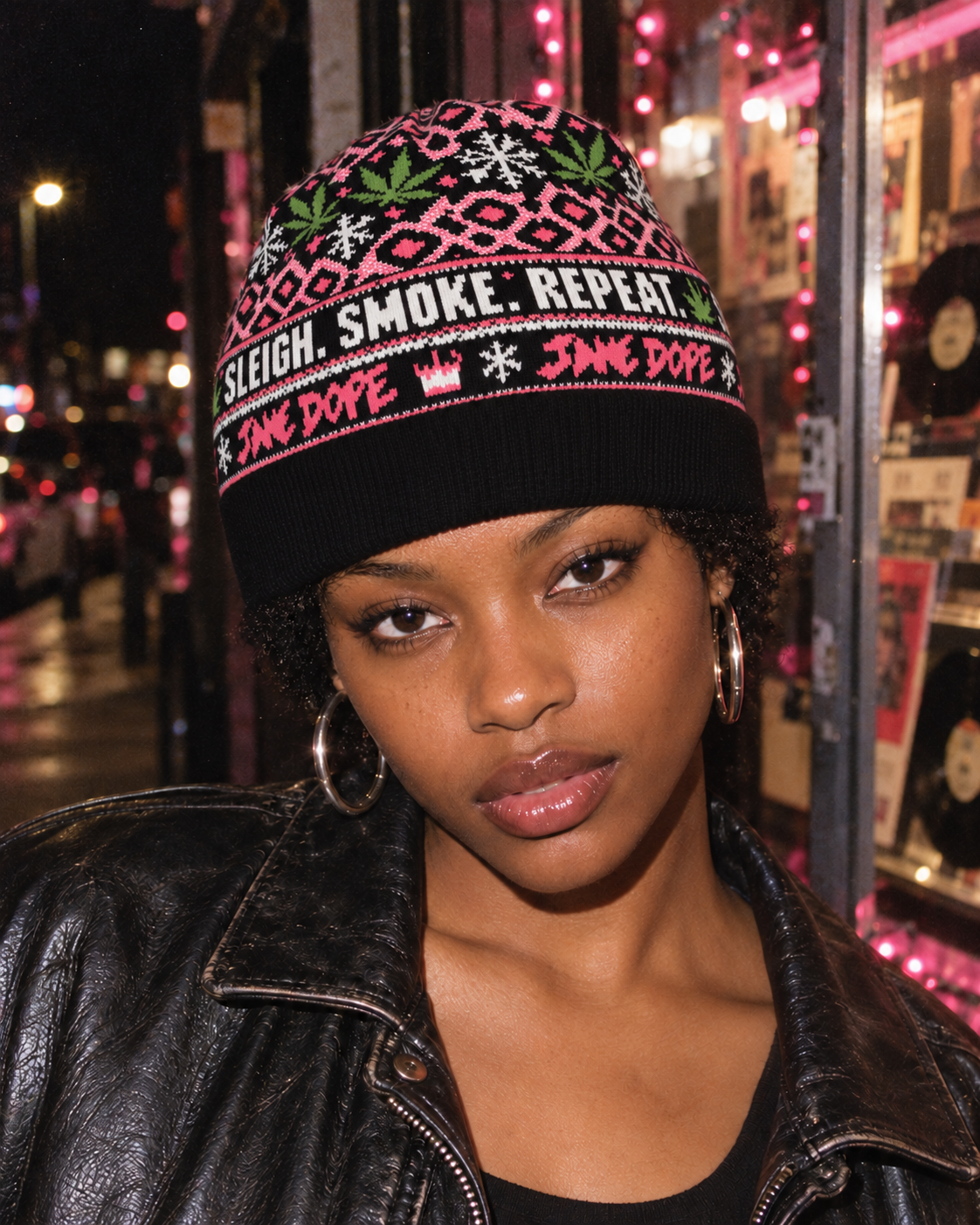 Sleigh Smoke Repeat knit toque worn snugly with a black leather jacket in a flash-lit holiday street portrait.