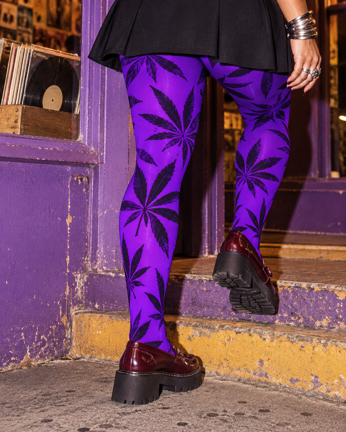 Close rear view of purple Herb-print tights and burgundy loafers, with one foot lifted onto a storefront step.