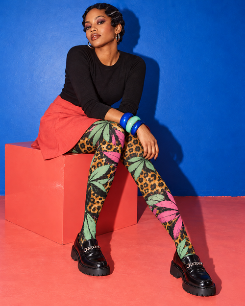 Runtz pink and mint botanical leopard tights, seated on a coral cube with black loafers. AI editorial illustration; styling accessories not included.