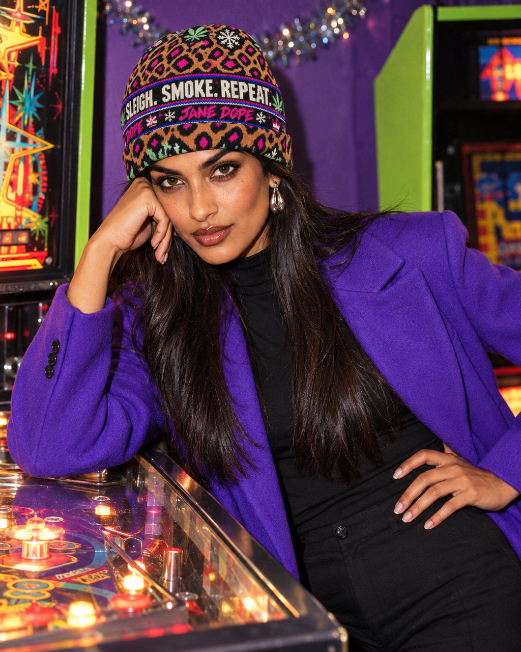 All-Over Print Knitted Hat with leopard print and Sleigh. Smoke. Repeat. lettering, worn with a violet coat in an arcade
