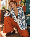 Jane Dope Soft Sativa navy botanical blazer on white, crouching beside a teal filing cabinet in orange trousers.