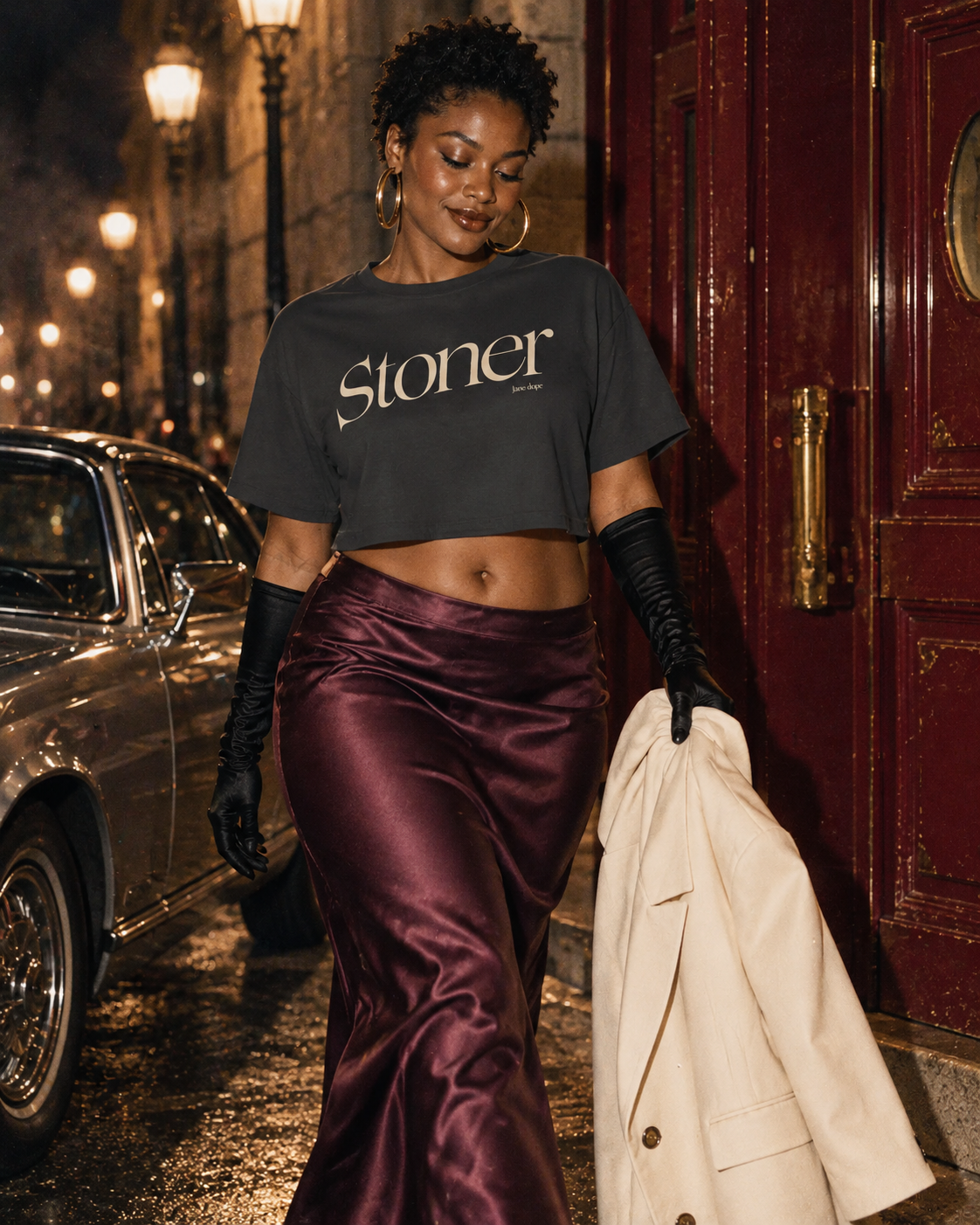 Stoner Diop cream graphic crop tee styled with a plum satin skirt, black gloves and an ivory coat.