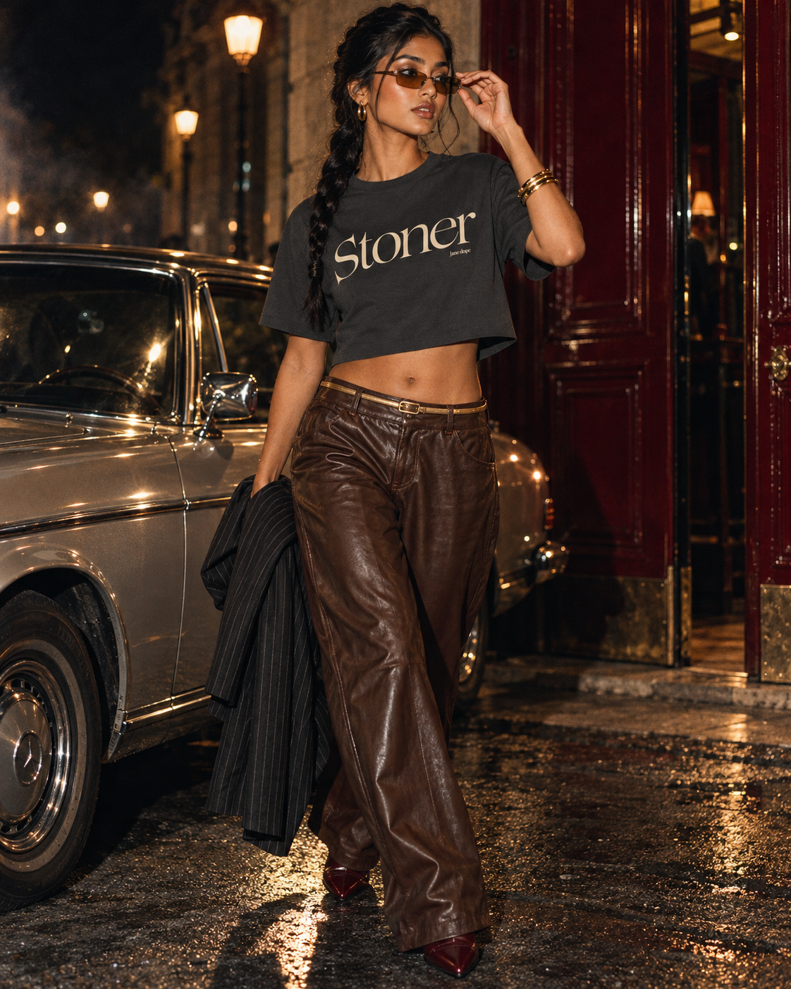 Front view of the Stoner Diop cropped tee with brown leather trousers as a model adjusts amber sunglasses.