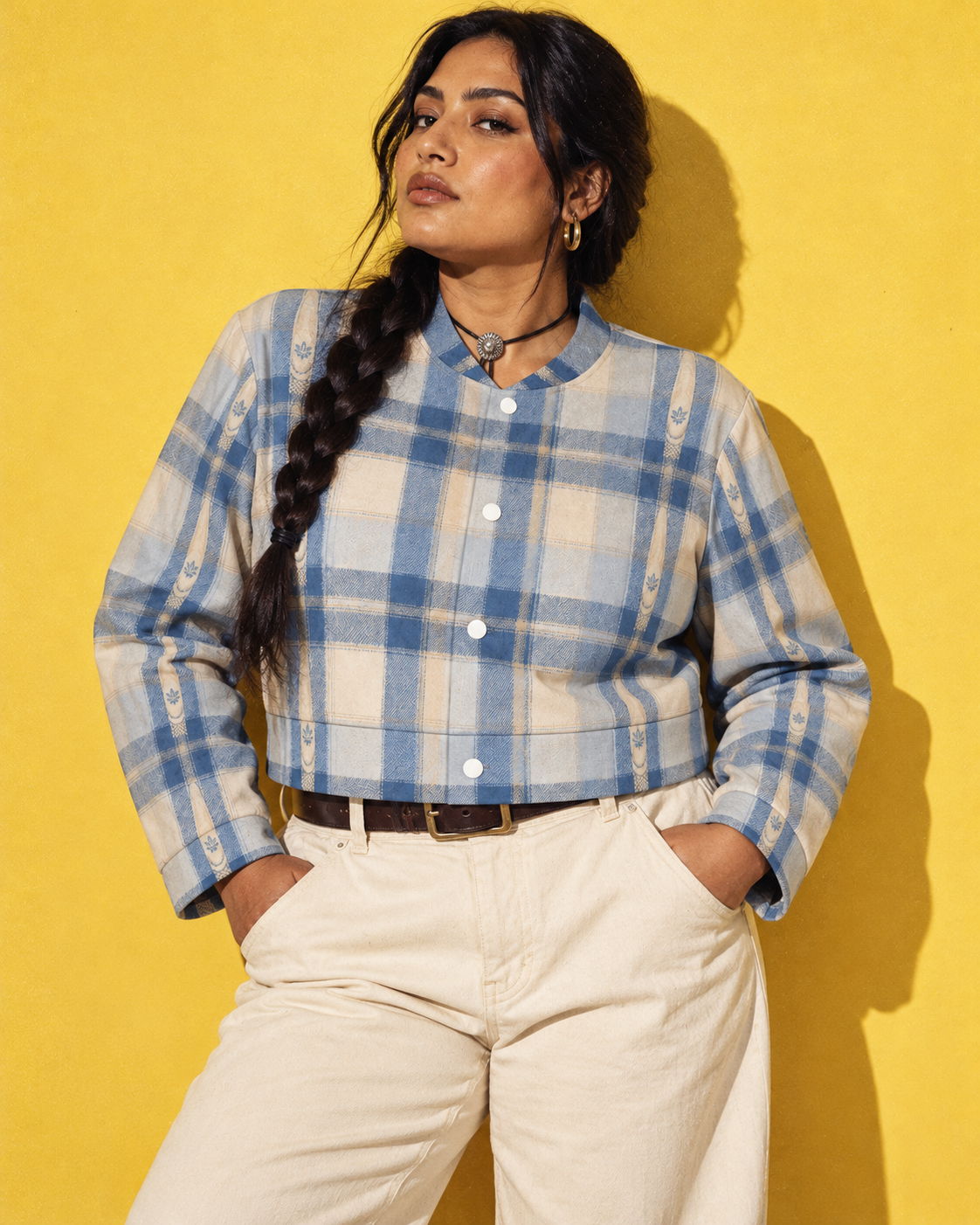 Sunday Sesh blue-and-cream cropped jacket, closed front with ecru denim and a leather belt against a yellow wall.