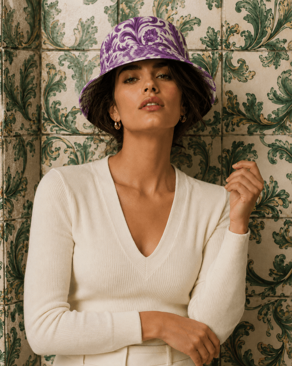 Woman wearing a purple patterned hat and white sweater against a decorative tiled wall.