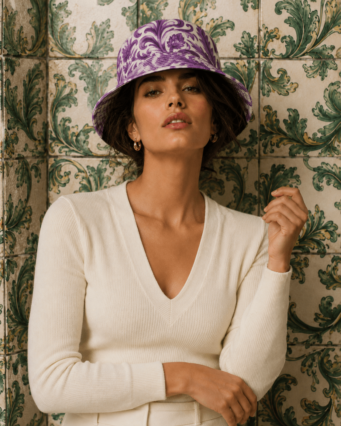 Woman wearing a purple patterned hat and white sweater against a decorative tiled wall.