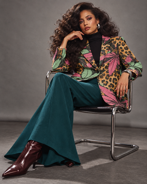 Runtz botanical leopard-print blazer styled with teal flares, seated on a chrome chair. AI editorial illustration; styling accessories not included.