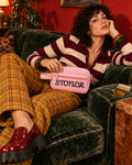 Pink STONER corduroy stash pouch on a model reclining across an emerald sofa in striped knitwear and mustard plaid trousers.