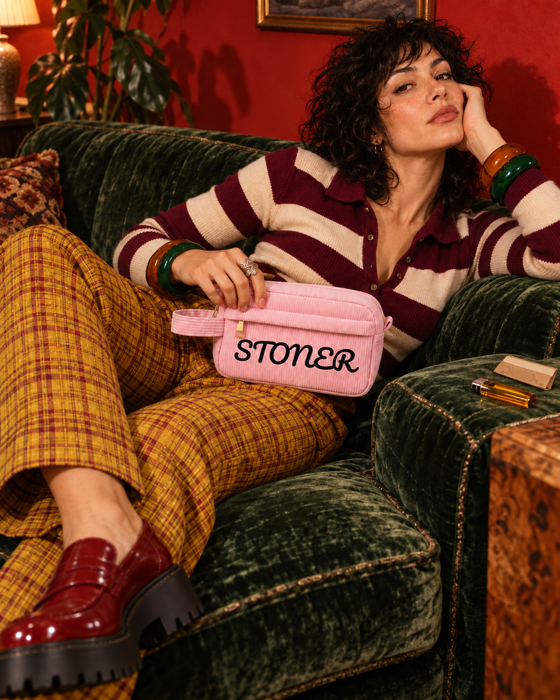 Pink STONER corduroy stash pouch on a model reclining across an emerald sofa in striped knitwear and mustard plaid trousers.